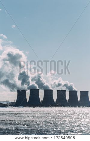 Cooling towers of a Nuclear Power Plant or NPP with thick smoke on blue sky background in sunny day. Copy space for text. Vertical image
