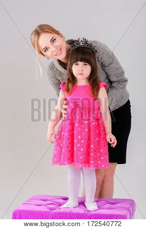 beautiful little girl in pink Princess dress with a crown and beautiful mother hugging on a gray background.