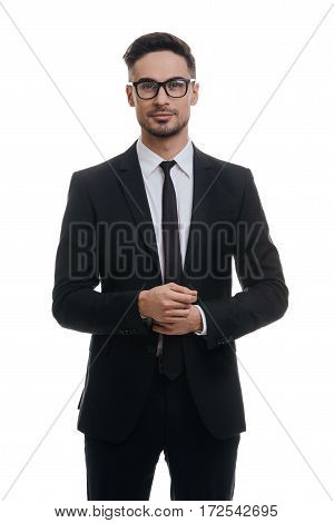 Portrait of style. Handsome young man in full suit adjusting his sleeve and looking at camera with smile while standing against white background