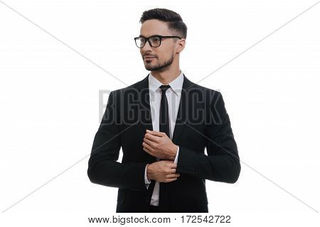 Used to look perfect. Handsome young man in full suit adjusting his sleeve and looking away while standing against white background