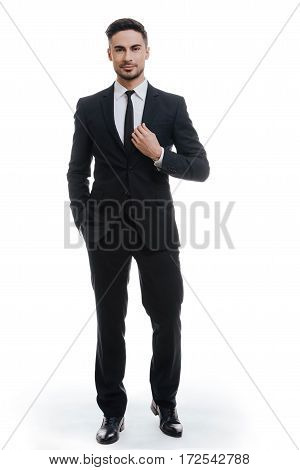 Portrait of elegance. Full length of handsome young man in full suit adjusting his jacket and holding one hand in pocket while standing against white background