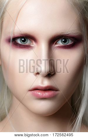 Beauty portrait of young woman with white brows and hair. Perfect skin and fashion makeup. Red smokey eyes. Studio shot. Sensuality passion trendy youth makeup concept.