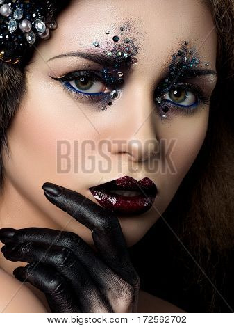 Beauty portrait of young woman with fashion makeup with rhinestones. Black hand and dark red lips. Studio shot.