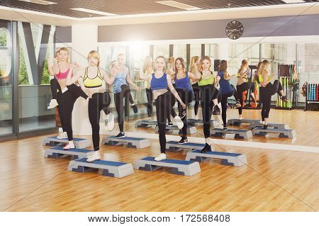 Group of young women in fitness class do step aerobics. Girls at step do leg kicks. Healthy lifestyle at gym studio. Slimming workout