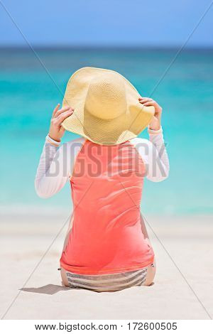 back view of young woman in rashguard and sunhat enjoying sunbathing at beautiful caribbean island sun protection and summer vacation concept