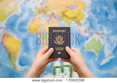 Child's hand holding US passport. Map background. Ready for traveling. Open world.