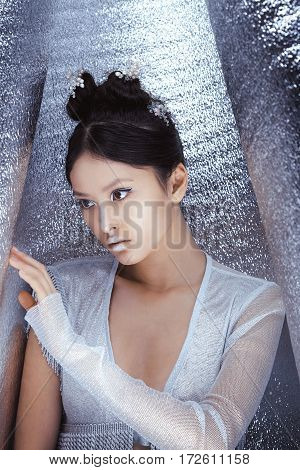 Portrait of futuristic young woman. Beautiful young multi-racial asian caucasian model cyber girl in silver urban clothes with conceptual hairstyle and make-up in metallik silver capsule. Sci-fi poster style.