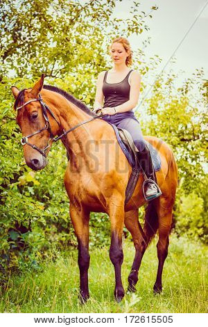 Animal horsemanship concept. Young woman sitting and ridding on a horse through garden on sunny spring day