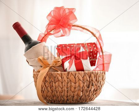 Wine bottle with gift boxes in wicker basket on light background