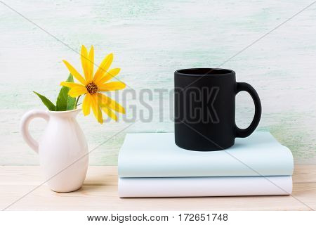 Black coffee mug mockup with yellow rosinweed flowers in pitcher. Empty mug mock up for brand promotion.