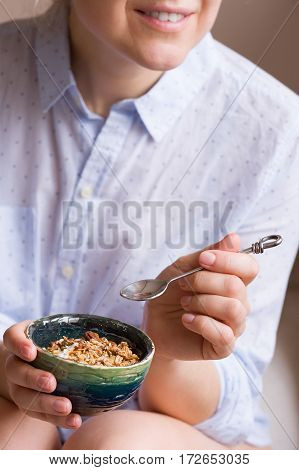 Young woman with muesli bowl. Girl eating breakfast cereals with nuts pumpkin seeds oats and yogurt in bowl. Girl holding homemade granola. Healthy snack or breakfst in the morning.