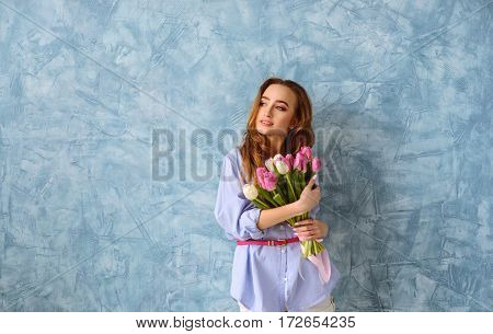 pretty young woman with bouquet of tulips on the blue wall background. Wide shot with copy space