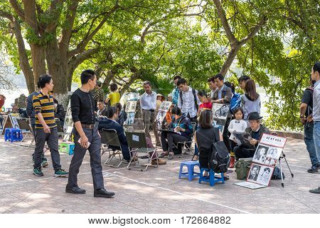 Hanoi Vietnam - February 17 2016: Asian portrait painter drawing sketch of customer by pencil on the sidewalk of Hoan Kiem lake in Hanoi Vietnam