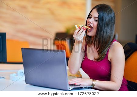 Young buisness woman eating pizza at the office.