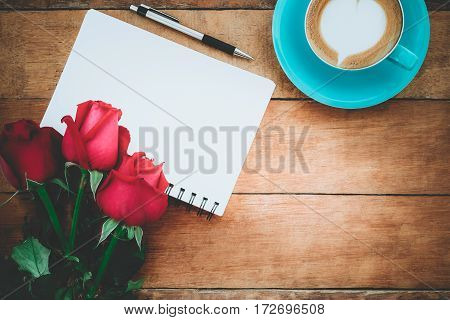 Red roses leather notebook pen and cup of coffee on wooden background with copy space.Valentines Day background concept Wedding day.Top view vintage tone