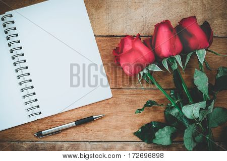Red roses leather notebook pen and cup of coffee on wooden background with copy space.Valentines Day background concept Wedding day.Top view vintage tone