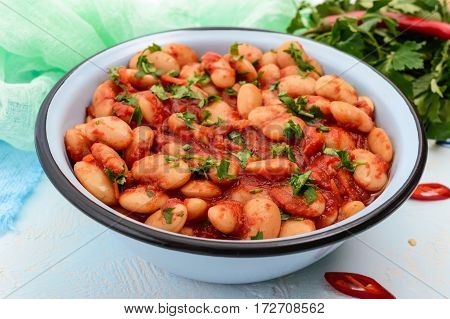 White large beans in sweet and sour tomato sauce in a bowl on a light background. The top view. Vegetarian cuisine. Lenten meal.