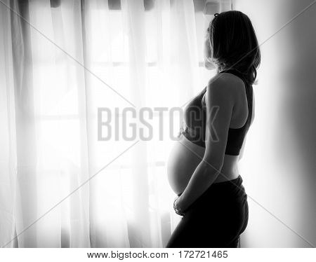 Pregnant woman looks at the street through the window