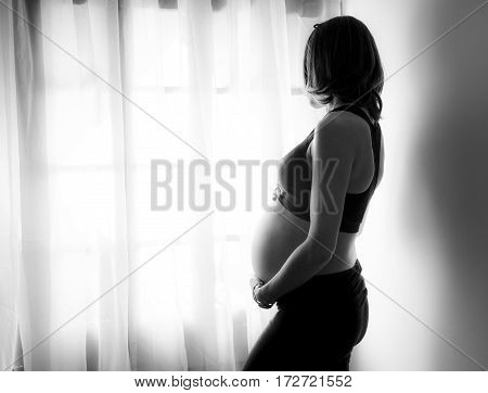 Pregnant woman looks at the street through the window