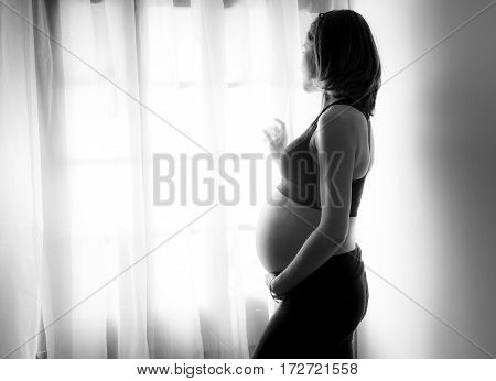 Pregnant woman looks at the street through the window