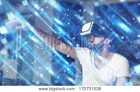 Young man with VR glasses playing virtual reality touching blue square polygons