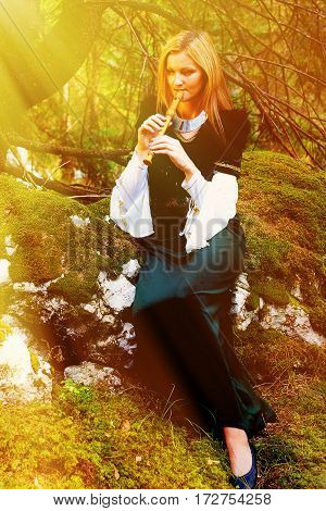 beautiful girl in a historical costume playing her flute in forest. Light effect