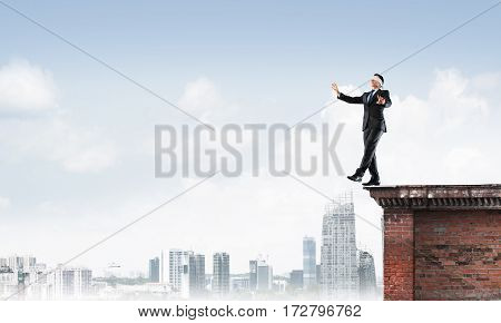 Businessman with blindfold on eyes walking off building top.