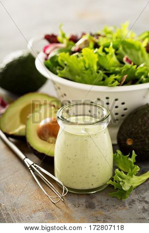 Avocado ranch dressing in small jar with salad leaves in a collander