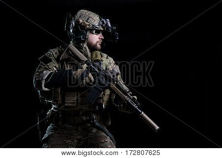 Special Forces soldier in helmet with night vision device and rifle on dark background