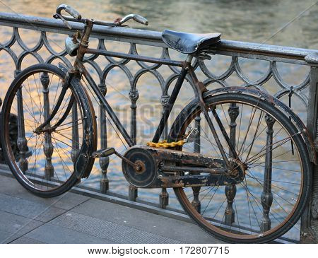 Black Old Bike Leaning On The Bridge Above The River