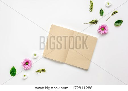 Flower petals and brown craftpaper copybook on white table background top view mock up