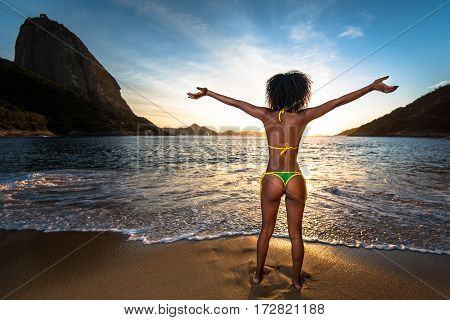 Sexy Brazilian Girl in Bikini Stands in the Beach With Open Arms and Welcomes A New Day in Rio de Janeiro With the Sugarloaf Mountain in the Background
