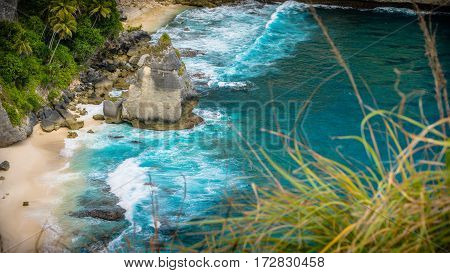 Rock in the ocean with beautiful palms behind at Atuh beach on Nusa Penida island, Indonesia.