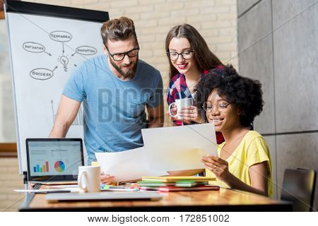 Multi ethnic coworkers dressed casually in colorful clothes working during the meeting at the office with laptop and documents