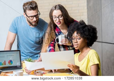 Multi ethnic coworkers dressed casually in colorful clothes working during the meeting at the office with laptop and documents