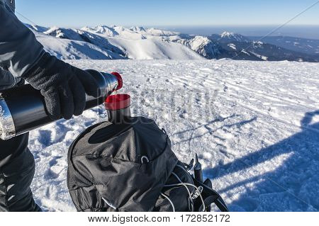 Pouring tea from a thermos into a cup in the winter at the top of the mountains.