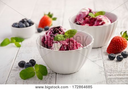 Ice cream with blueberries and strawberries in white bowl on white wooden background, selective focus