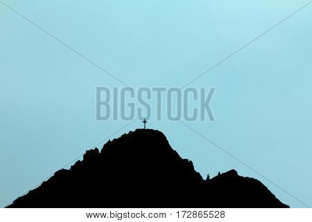 Graphical black silhouette of mountain peak with summit cross. Blue glowing background.