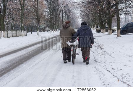 DNEPR UKRAINE - JANUARY 02 2017: Elderly pair walking on a winter street rolling old bicycle loaded with bags in Dnepr city Ukraine at January 02,2017