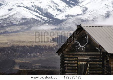 Old cabin with snow covered mountains in background and elk antlers