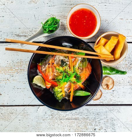 Asian prawns with rice noodles and spring rools, top view, served on old wooden planks.