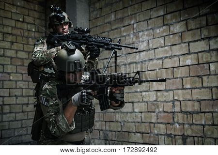 Pair of US Army Rangers with machinegun and rifle moving along the wall after each other on military mission