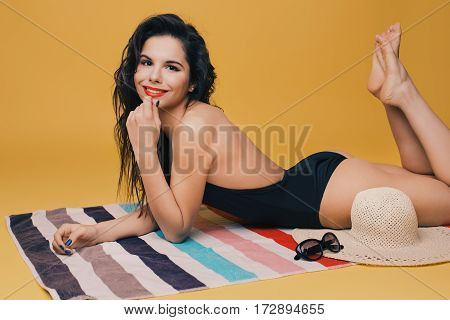 Fashion photo of beautiful and young lady in swimsuits posing in studio, is resting on a colorful towel