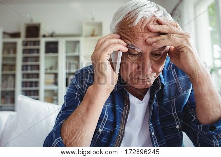 Tensed senior man talking on mobile phone at home