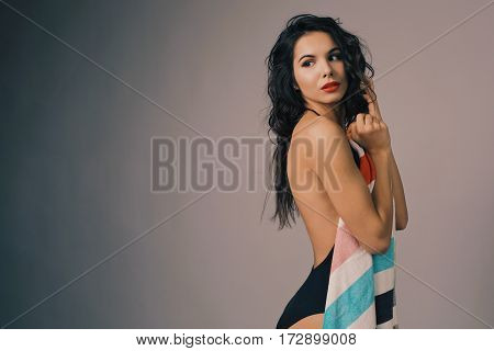 Fashion photo of beautiful and young lady in swimsuits posing in studio, holding colorful towel
