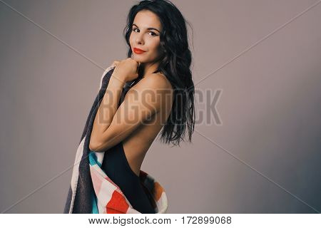 Fashion photo of beautiful and young lady in swimsuits posing in studio, holding colorful towel