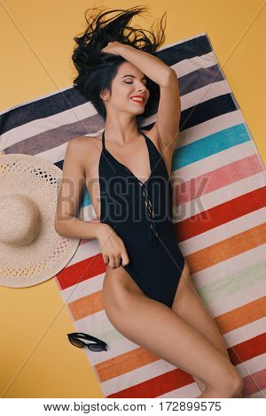 Fashion photo of beautiful and young lady in swimsuits posing in studio, is resting on a colorful towel