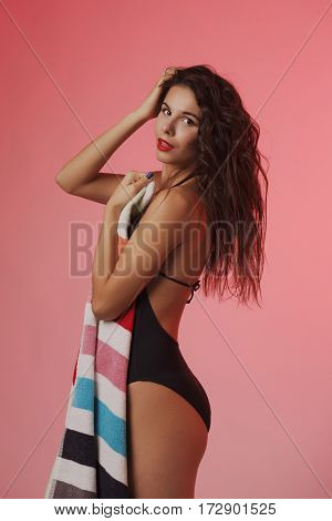 Fashion photo of beautiful and young lady in swimsuits posing in studio, holding colorful towel