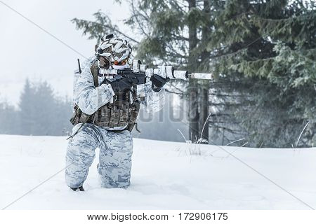 Winter arctic mountains warfare. Action in cold conditions. Trooper with weapons in forest somewhere above the Arctic Circle on one knee