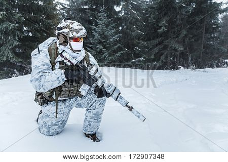 Winter arctic mountains warfare. Action in cold conditions. Trooper with weapons in forest somewhere above the Arctic Circle on one knee